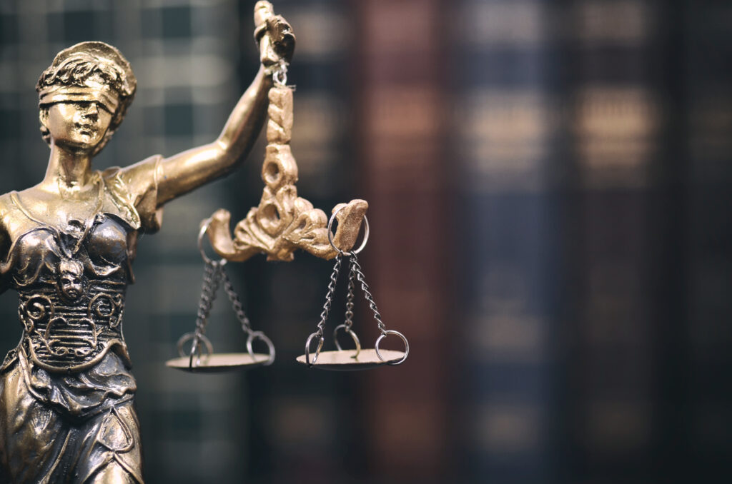 Scales of Justice and handcuffs on a black wooden background.